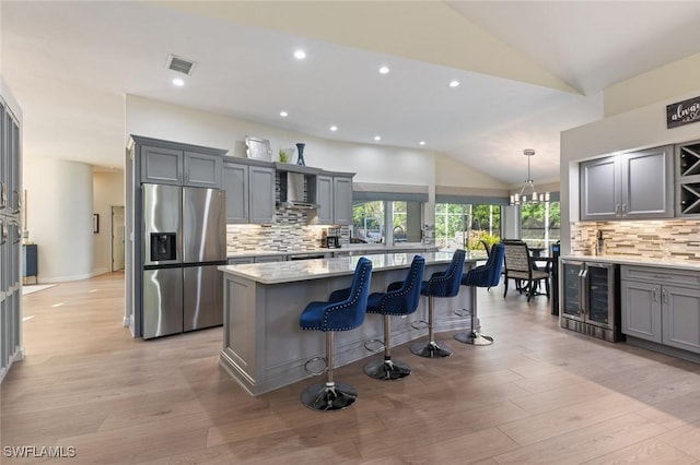 kitchen with visible vents, wine cooler, stainless steel refrigerator with ice dispenser, wall chimney exhaust hood, and a center island