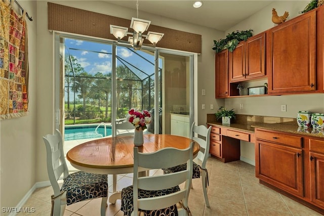 dining room featuring baseboards, light tile patterned floors, built in desk, an inviting chandelier, and a sunroom