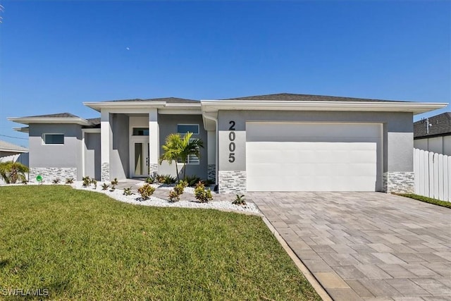 prairie-style house with an attached garage, stucco siding, a front lawn, stone siding, and decorative driveway