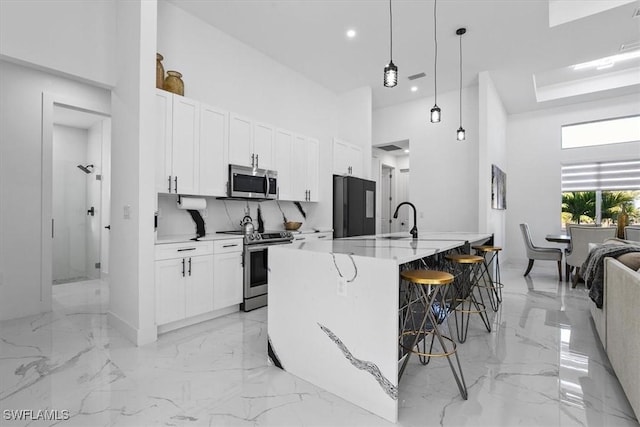 kitchen featuring white cabinetry, a kitchen breakfast bar, a towering ceiling, marble finish floor, and stainless steel appliances