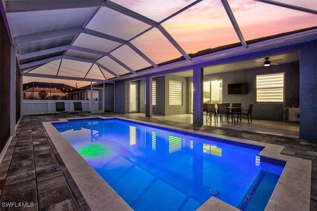 outdoor pool with glass enclosure, a ceiling fan, and a patio