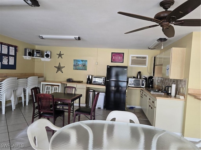 kitchen featuring tile patterned floors, stainless steel microwave, freestanding refrigerator, and a sink