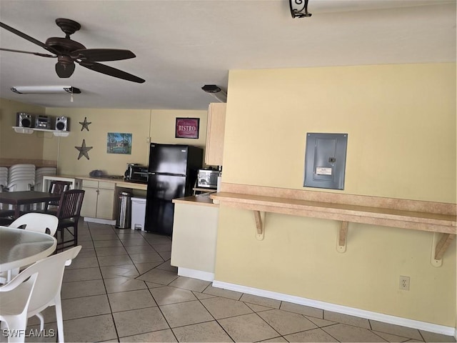 kitchen featuring light tile patterned floors, stainless steel microwave, a kitchen breakfast bar, and freestanding refrigerator