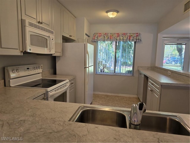 kitchen with a sink, baseboards, white appliances, and a healthy amount of sunlight