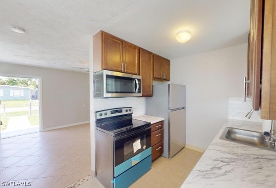 kitchen with baseboards, light countertops, appliances with stainless steel finishes, brown cabinets, and backsplash