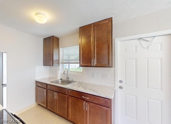 kitchen with brown cabinetry, baseboards, backsplash, and a sink