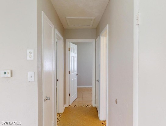 corridor featuring light tile patterned floors and attic access