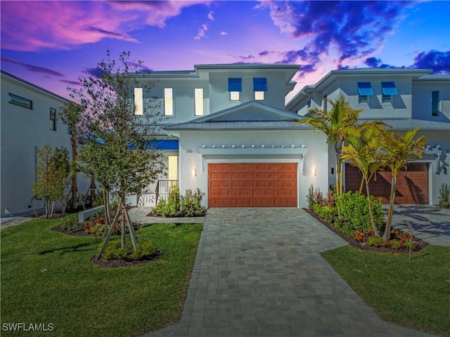 view of front facade featuring a garage, a yard, decorative driveway, and stucco siding