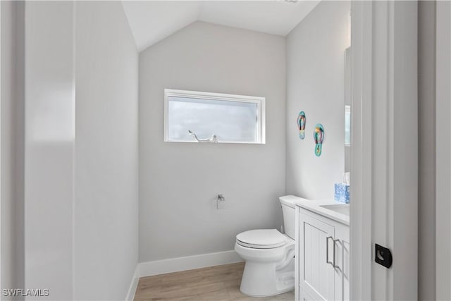 bathroom featuring baseboards, toilet, lofted ceiling, wood finished floors, and vanity