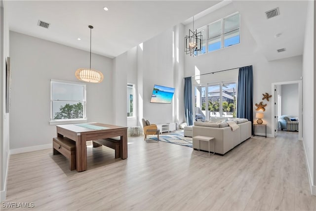 living room featuring baseboards, visible vents, a towering ceiling, and light wood finished floors