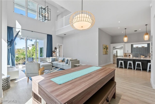 dining area featuring baseboards, a high ceiling, light wood-style floors, a chandelier, and recessed lighting