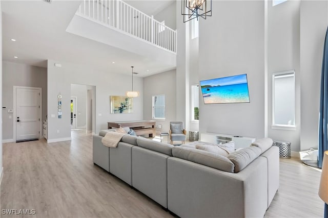 living area featuring a chandelier, light wood-type flooring, a towering ceiling, and baseboards