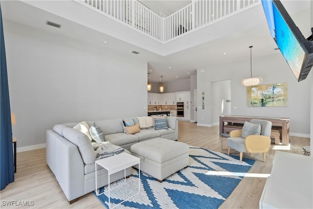 living area featuring light wood finished floors, a high ceiling, visible vents, and baseboards