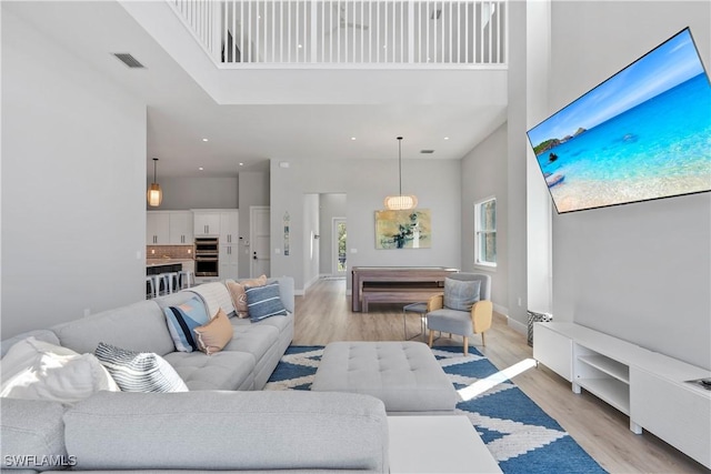 living room with light wood-type flooring, baseboards, a high ceiling, and visible vents