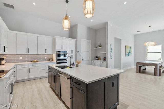 kitchen with light wood-type flooring, appliances with stainless steel finishes, decorative backsplash, and a sink