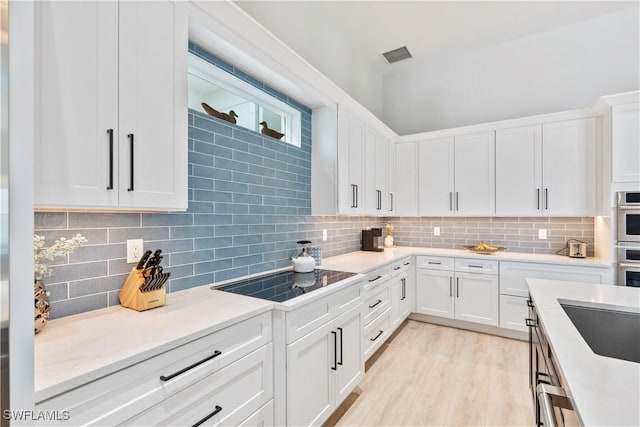 kitchen featuring black electric stovetop, visible vents, backsplash, light wood-style floors, and white cabinetry