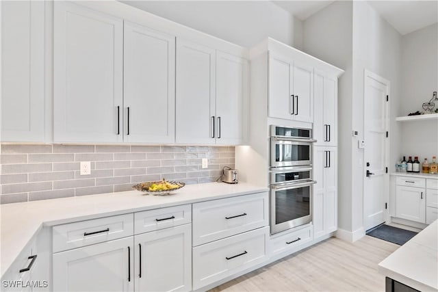 kitchen featuring light countertops, light wood-style floors, double oven, white cabinetry, and backsplash