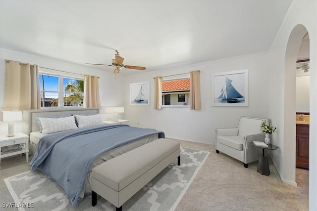 bedroom with light colored carpet, arched walkways, and ceiling fan