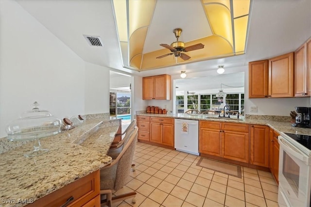 kitchen with visible vents, a sink, light stone counters, white appliances, and a raised ceiling