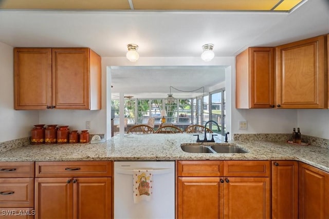 kitchen with a sink, light stone counters, brown cabinetry, and white dishwasher