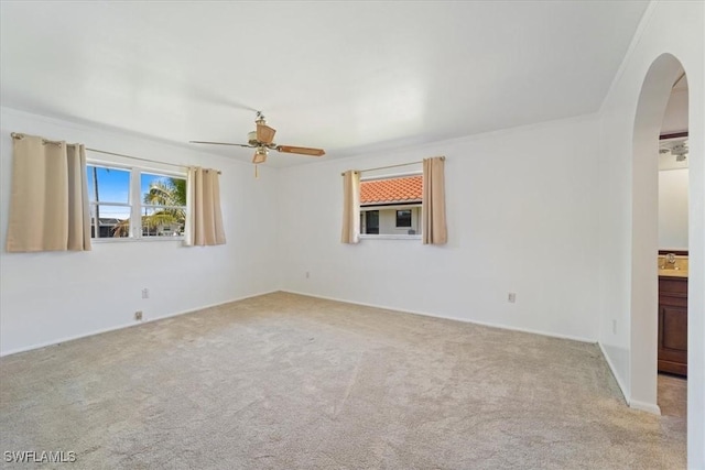 unfurnished room featuring arched walkways, light colored carpet, and ceiling fan