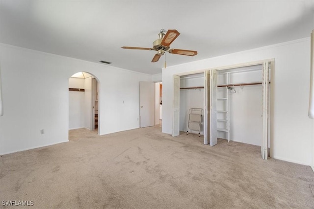 unfurnished bedroom with visible vents, multiple closets, ornamental molding, carpet flooring, and arched walkways