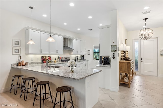 4360 Aurora St, Naples, FL 34119 - kitchen with wall chimney range hood, a peninsula, a kitchen bar, light tile patterned floors, and white cabinetry