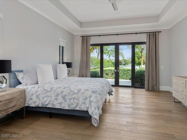 bedroom featuring a tray ceiling, wood finished floors, access to exterior, and french doors