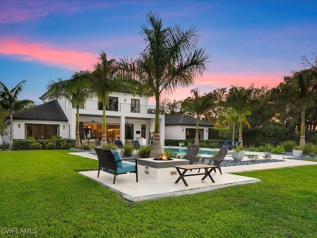 back of property with a patio, a balcony, an outdoor pool, a fire pit, and a lawn