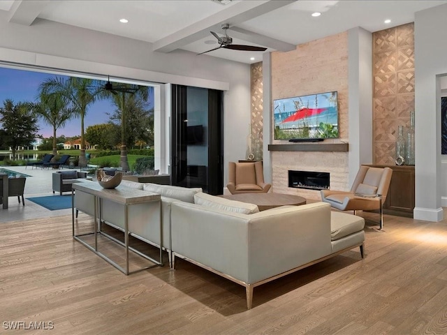 living area featuring light wood-type flooring, beam ceiling, a stone fireplace, recessed lighting, and a ceiling fan