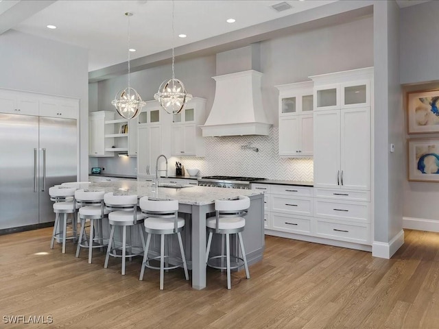 kitchen with a center island with sink, light wood-style flooring, custom exhaust hood, stainless steel appliances, and a sink