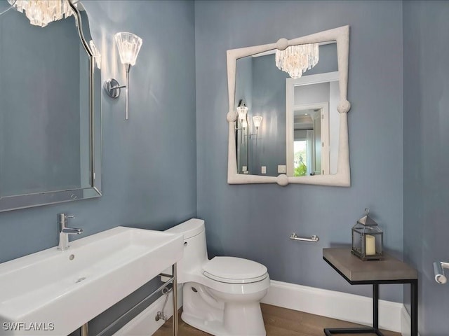 half bathroom with wood finished floors, baseboards, a sink, toilet, and a chandelier