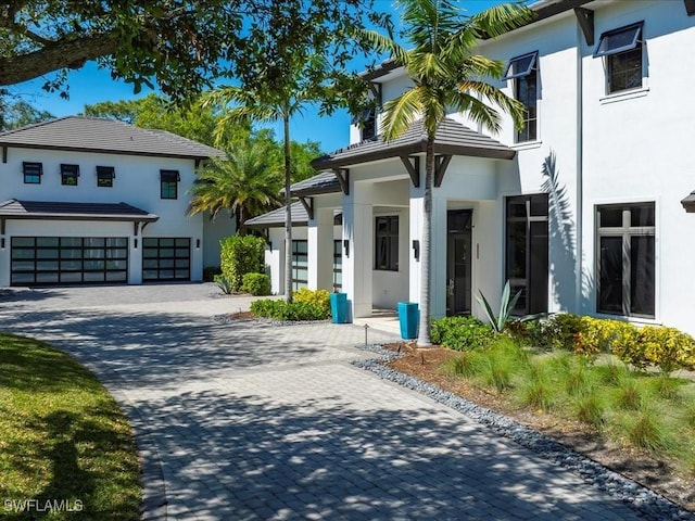 view of front of house with decorative driveway, an attached garage, and stucco siding