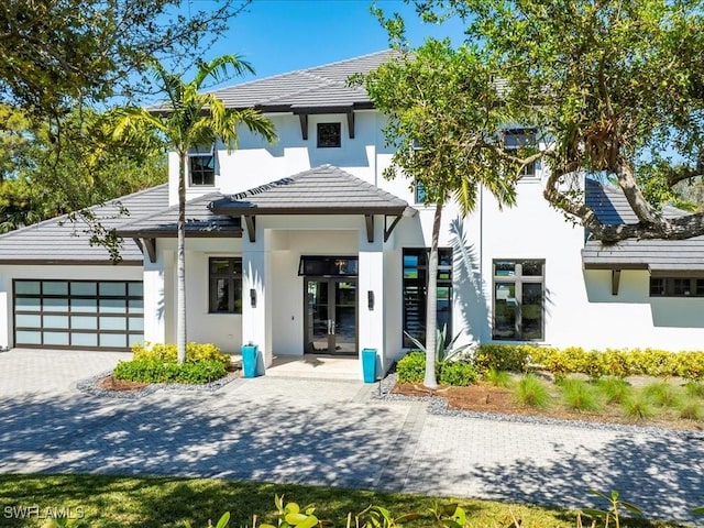 rear view of property with stucco siding, a tile roof, decorative driveway, french doors, and an attached garage