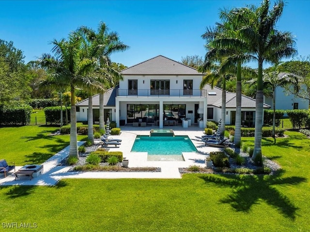 rear view of house with a pool with connected hot tub, a patio, a yard, an outdoor living space with a fire pit, and a balcony