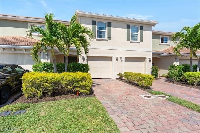 view of front of house featuring a tiled roof, decorative driveway, a garage, and stucco siding