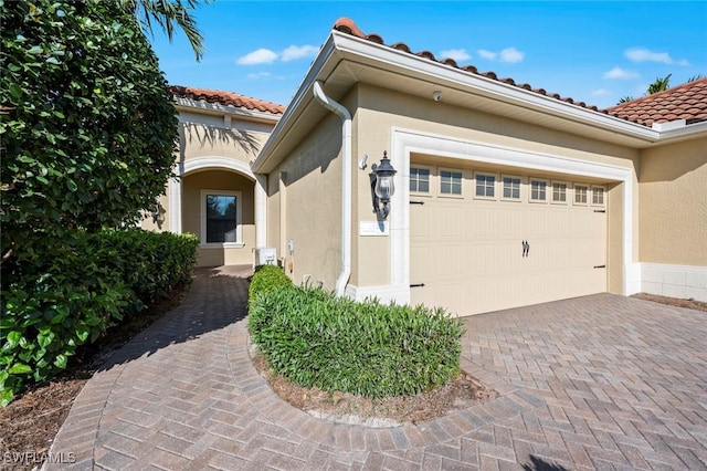 exterior space featuring stucco siding, a tile roof, decorative driveway, and a garage