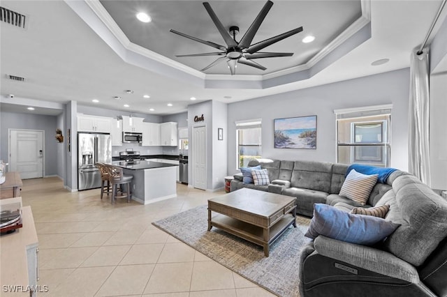 living area featuring visible vents, a tray ceiling, ornamental molding, light tile patterned floors, and a ceiling fan