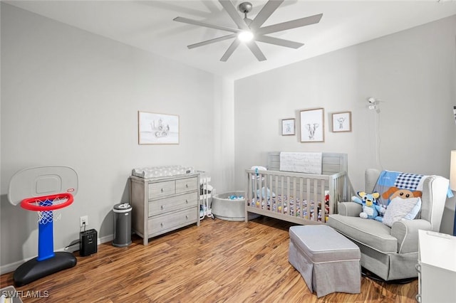 bedroom featuring baseboards, a nursery area, wood finished floors, and a ceiling fan