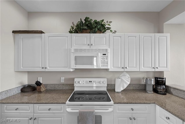 kitchen featuring dark stone counters, white appliances, and white cabinets