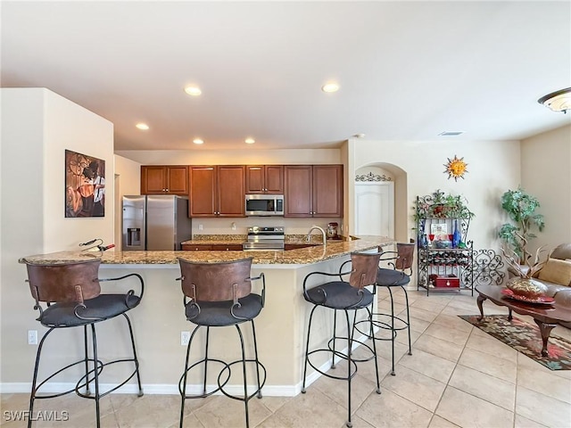 kitchen with a kitchen bar, a peninsula, light stone counters, and appliances with stainless steel finishes