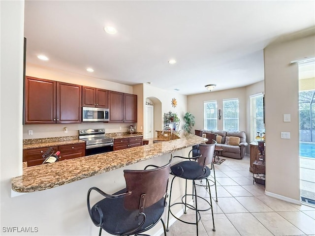 kitchen featuring open floor plan, light tile patterned floors, appliances with stainless steel finishes, a kitchen breakfast bar, and arched walkways