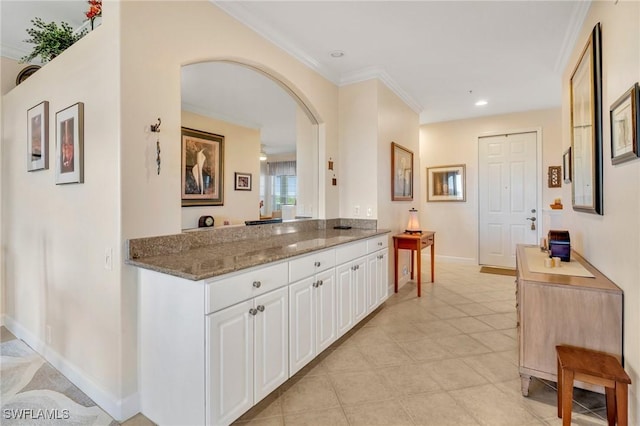 kitchen with baseboards, stone counters, arched walkways, white cabinetry, and crown molding