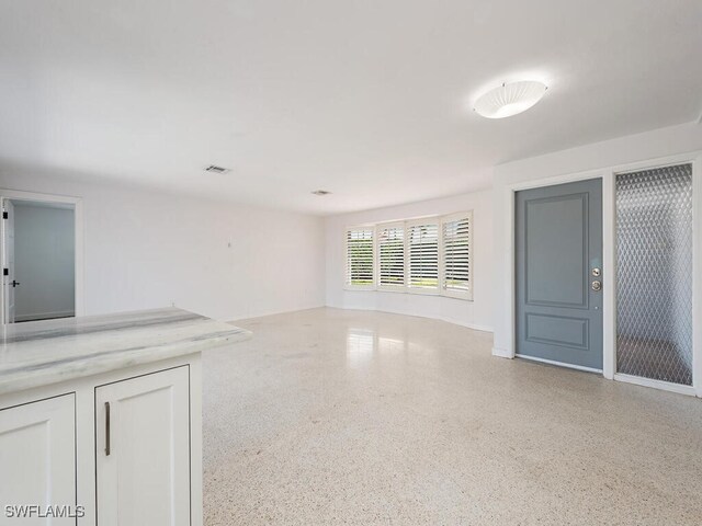 unfurnished living room with speckled floor and visible vents