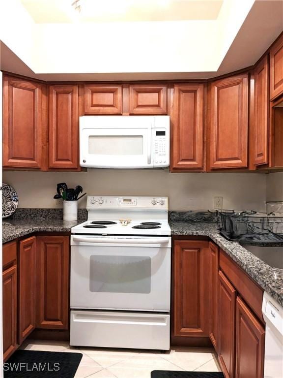 kitchen with brown cabinetry, white appliances, dark countertops, and a sink