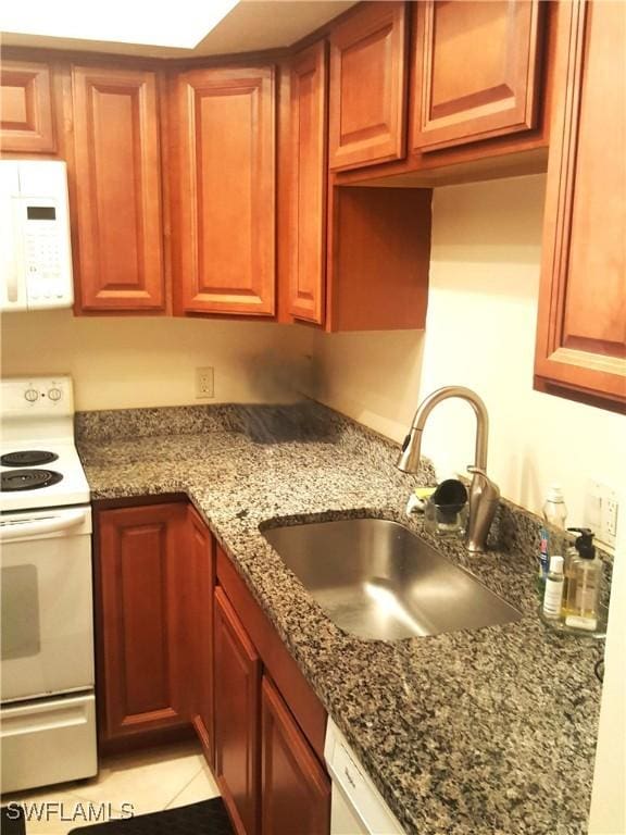 kitchen with light tile patterned floors, dark stone countertops, white appliances, and a sink