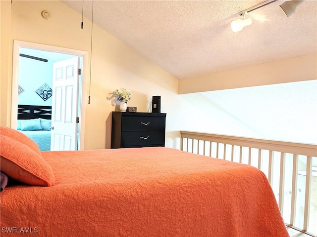 bedroom with track lighting, a textured ceiling, and vaulted ceiling