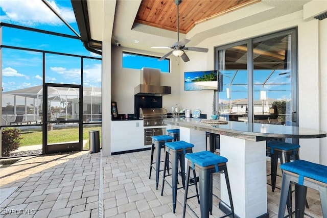 kitchen with a tray ceiling, a sunroom, wooden ceiling, and wall chimney range hood