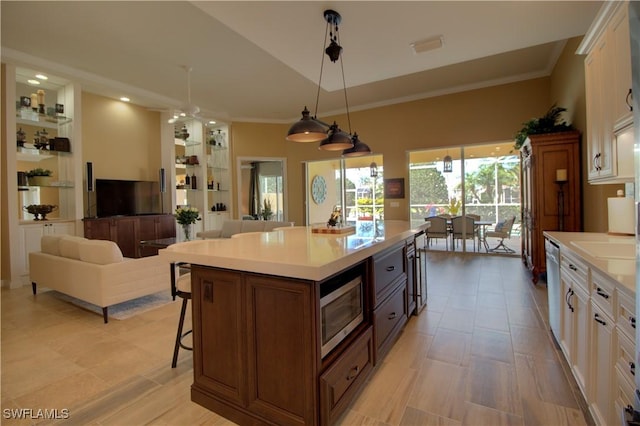 kitchen featuring stainless steel microwave, a breakfast bar, light countertops, ornamental molding, and white cabinets