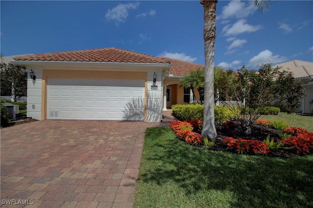 mediterranean / spanish house featuring a tiled roof, central AC unit, stucco siding, decorative driveway, and an attached garage